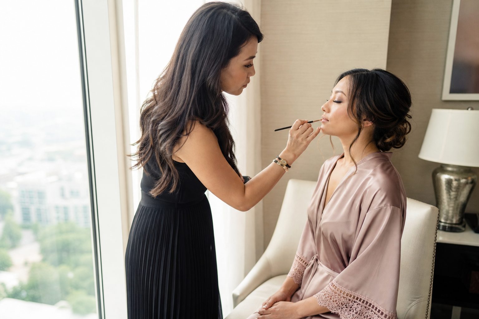 Bridal makeup artist working beside a bright window in a light filled hotel suite on a wedding morning
